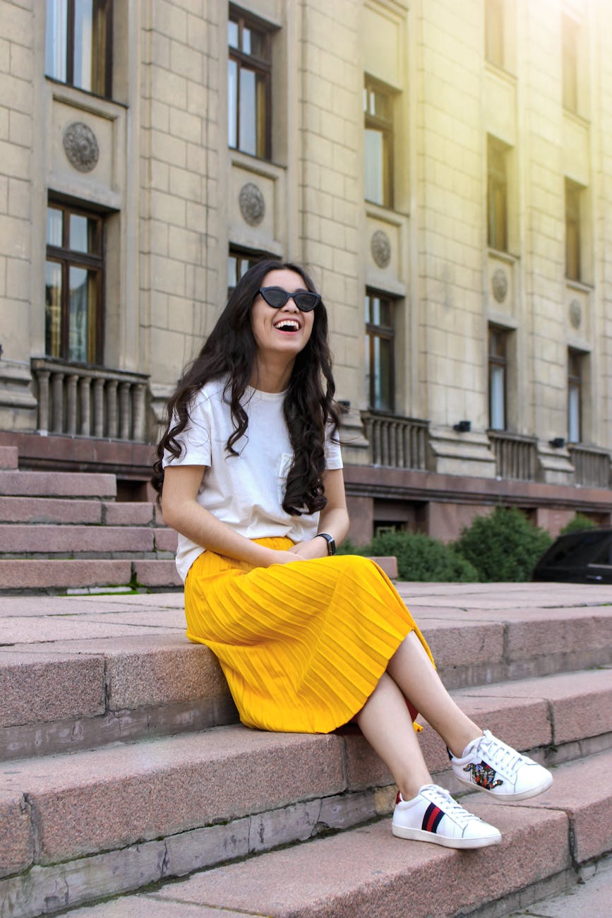 woman wearing white shirt and yellow skirt sitting on brown concrete brick stairs